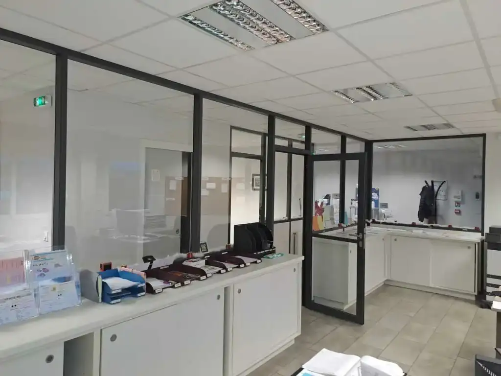 Aménagement de bureau moderne avec cloisons vitrées Bureau avec cloisons vitrées, comptoirs blancs et dossiers organisés dans un espace de travail administratif moderne.