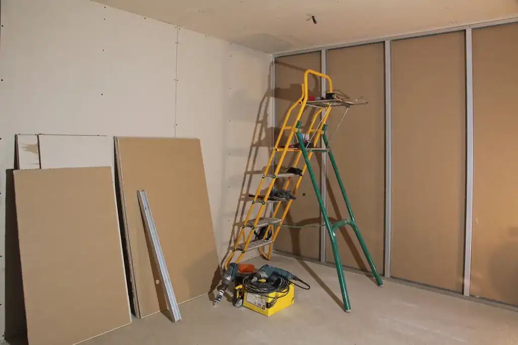 Pose de Cloisons Sèches : Chantier et Outils de Rénovation Chantier de rénovation avec plaques de plâtre, escabeau jaune et outils électriques pour pose de cloisons sèches.