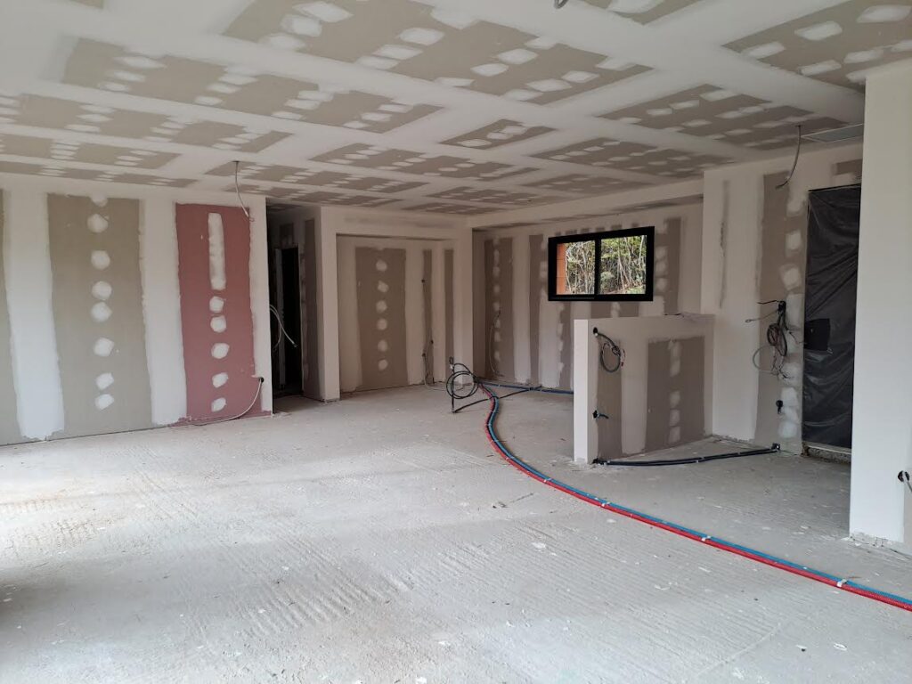 Travaux de plâtrerie et plomberie sur chantier intérieur Chantier de rénovation intérieure avec pose de plaques de plâtre, câbles électriques et tuyaux PEX apparents au sol.